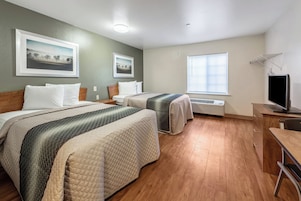 Quarto de hotel com duas camas, uma escrivaninha, televisão e janela com persianas.