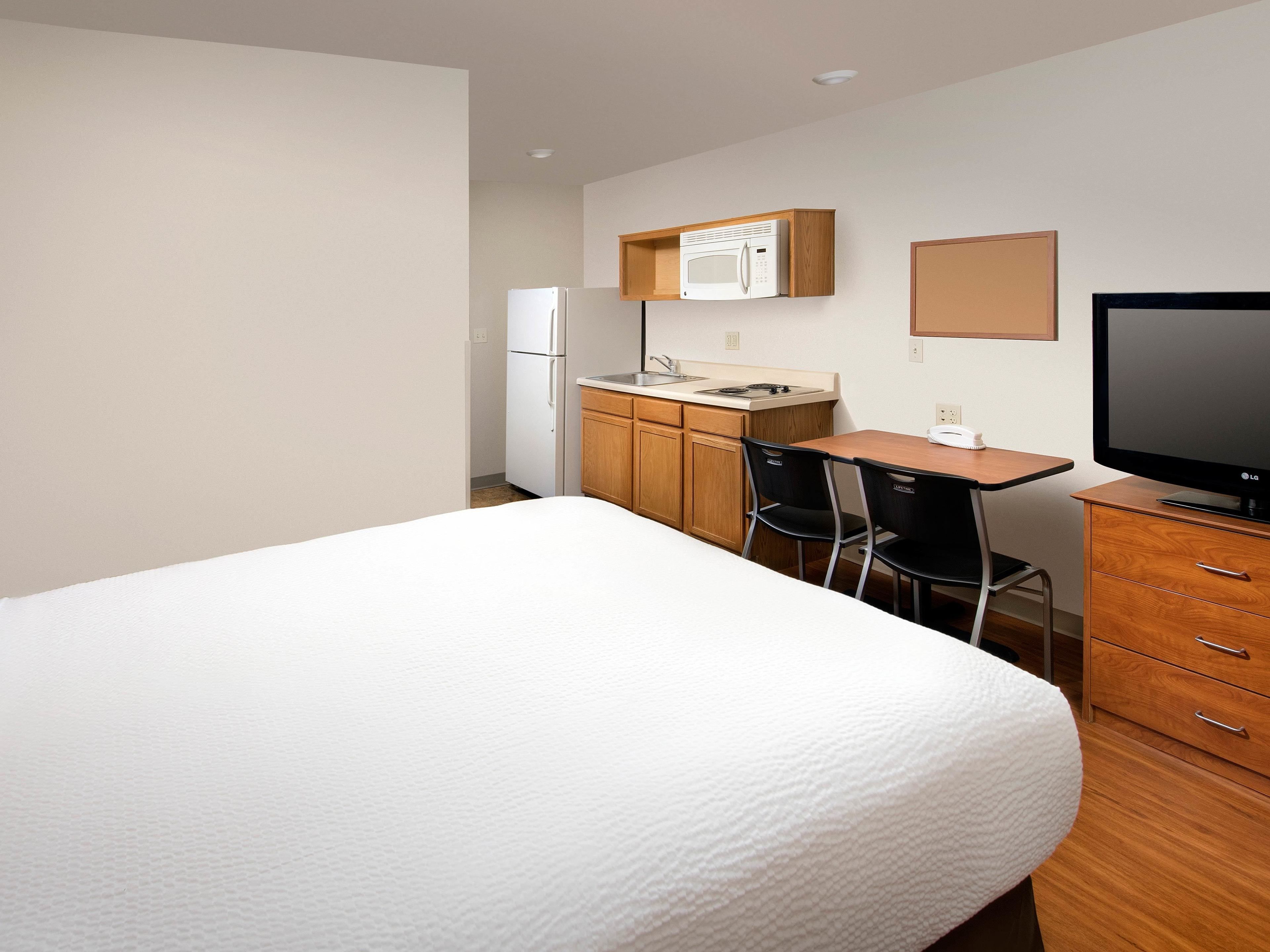 Une chambre d’hôtel équipée d’un lit, d’un bureau avec une chaise, d’un four à micro-ondes, d’un réfrigérateur et d’une télévision.