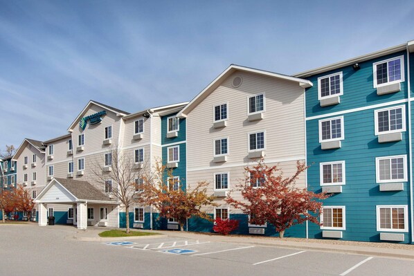 A multi-story hotel with a central entrance, air conditioning units, and a parking lot with handicapped parking. - WoodSpring Suites Council Bluffs (Council Bluffs)