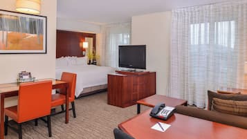 Una habitación de hotel con cama, escritorio con teléfono, televisor y zona de estar con sofá.