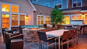 An outdoor patio with a stone fire pit, wicker furniture, and a view of the house. - Residence Inn by Marriott, North Conway (North Conway)
