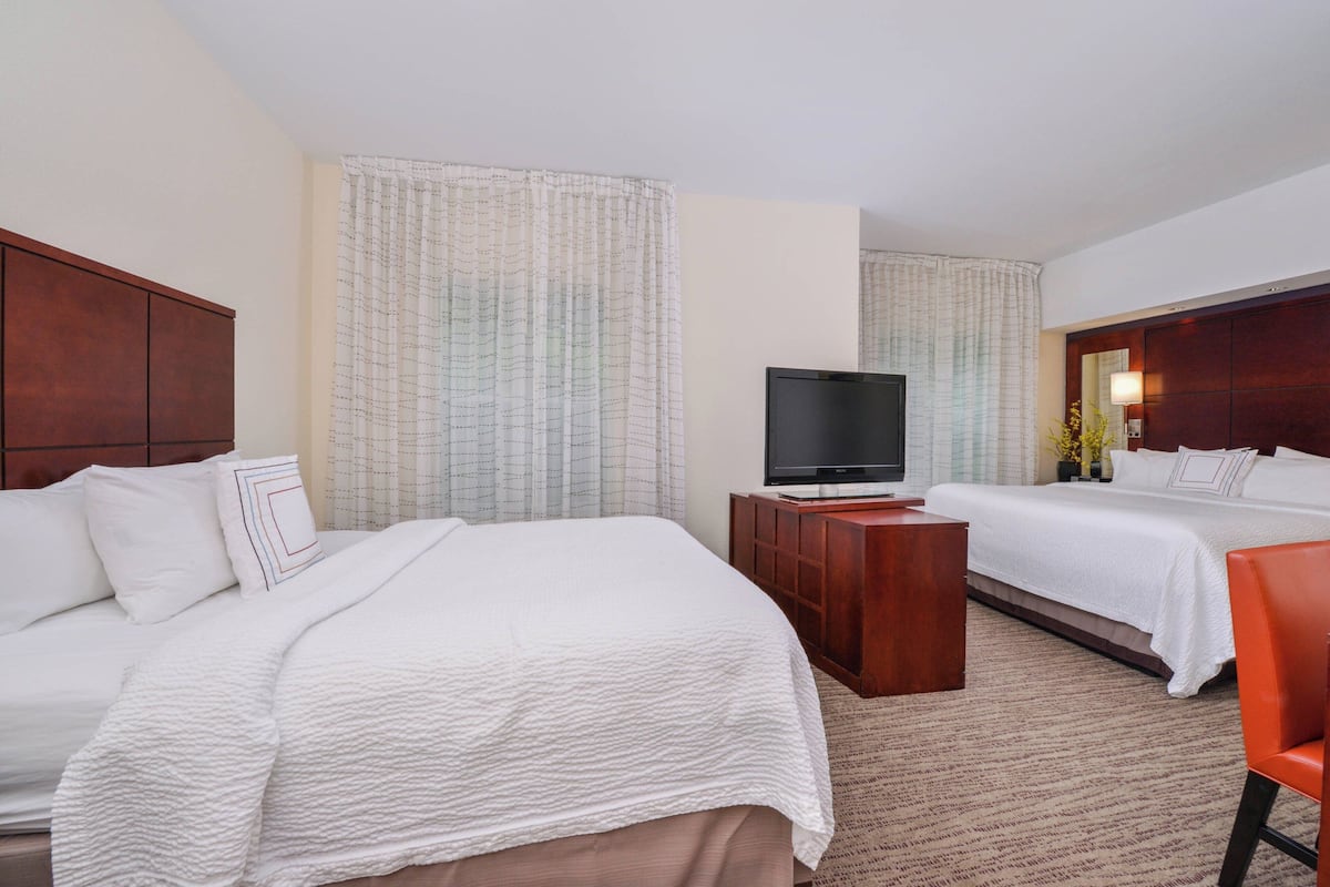 Quarto de hotel com duas camas, uma TV, uma escrivaninha de madeira e uma cadeira vermelha.