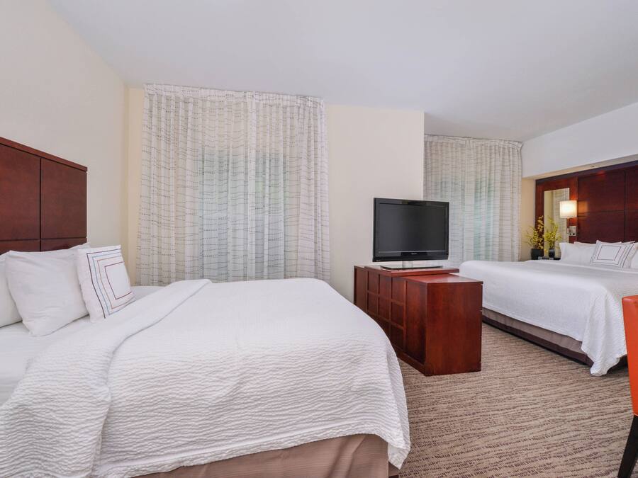 A hotel room with two beds, a TV, a wooden desk, and a red chair.