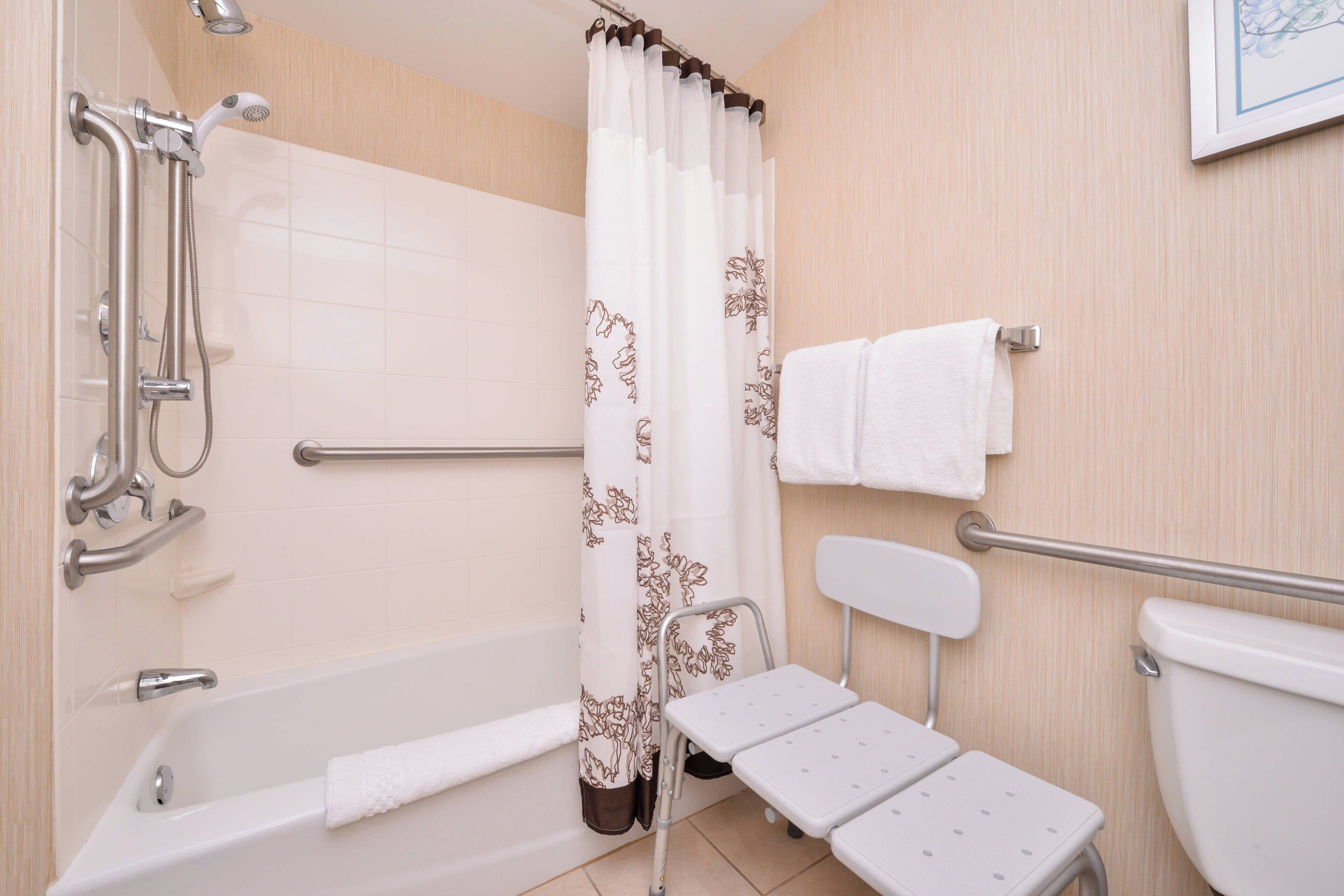 A bathroom with a bathtub, a shower with a curtain, a toilet, and a small white table.