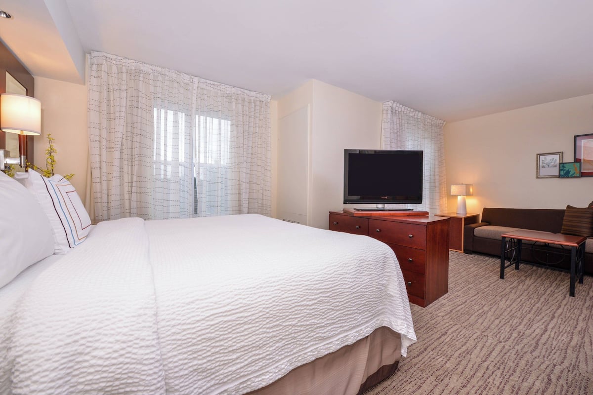Quarto de hotel com uma cama grande, televisão, escrivaninha e sofá.