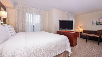A hotel room with a large bed, a TV, a desk, and a sofa.