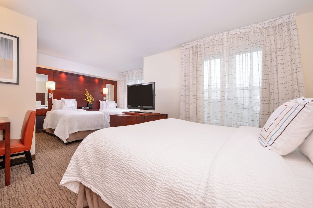 Quarto de hotel com duas camas, televisão, escrivaninha e uma cadeira.