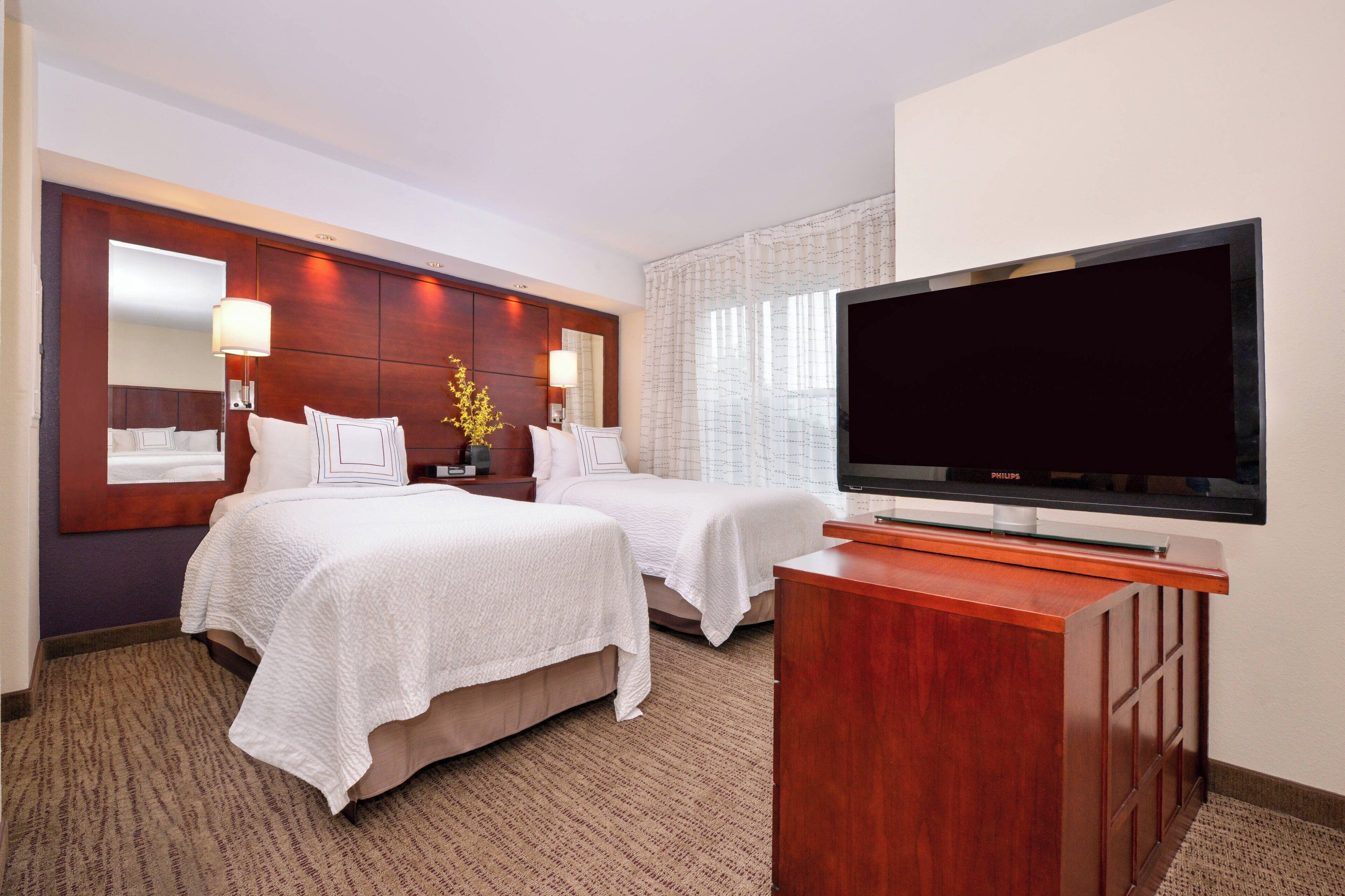 Habitación de hotel con dos camas, televisor, cabecero de madera y un ventanal grande con cortinas.