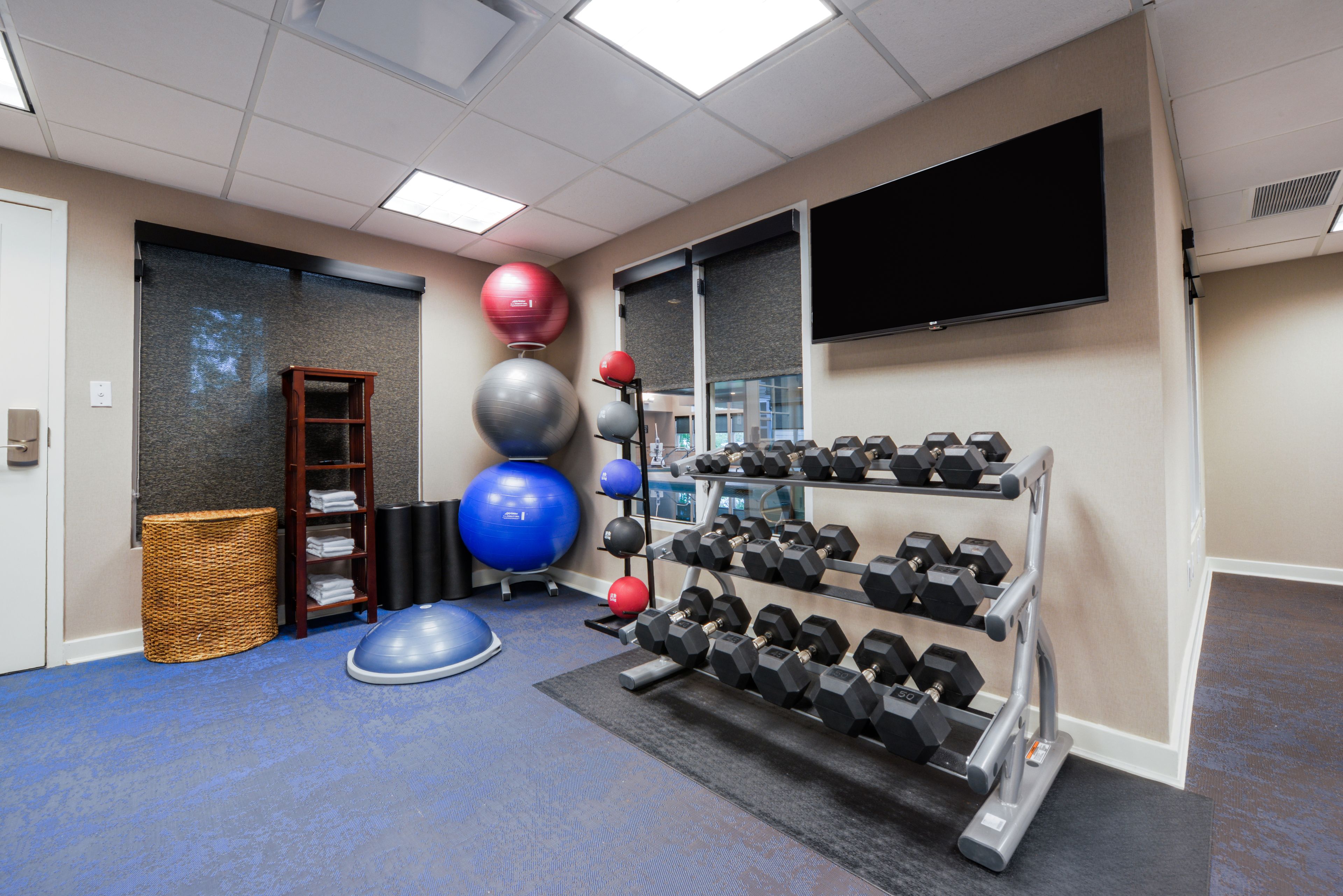 Ein Fitnessraum mit Trainingsgeräten, einem Fernseher und einem an der Wand befestigten Regal.