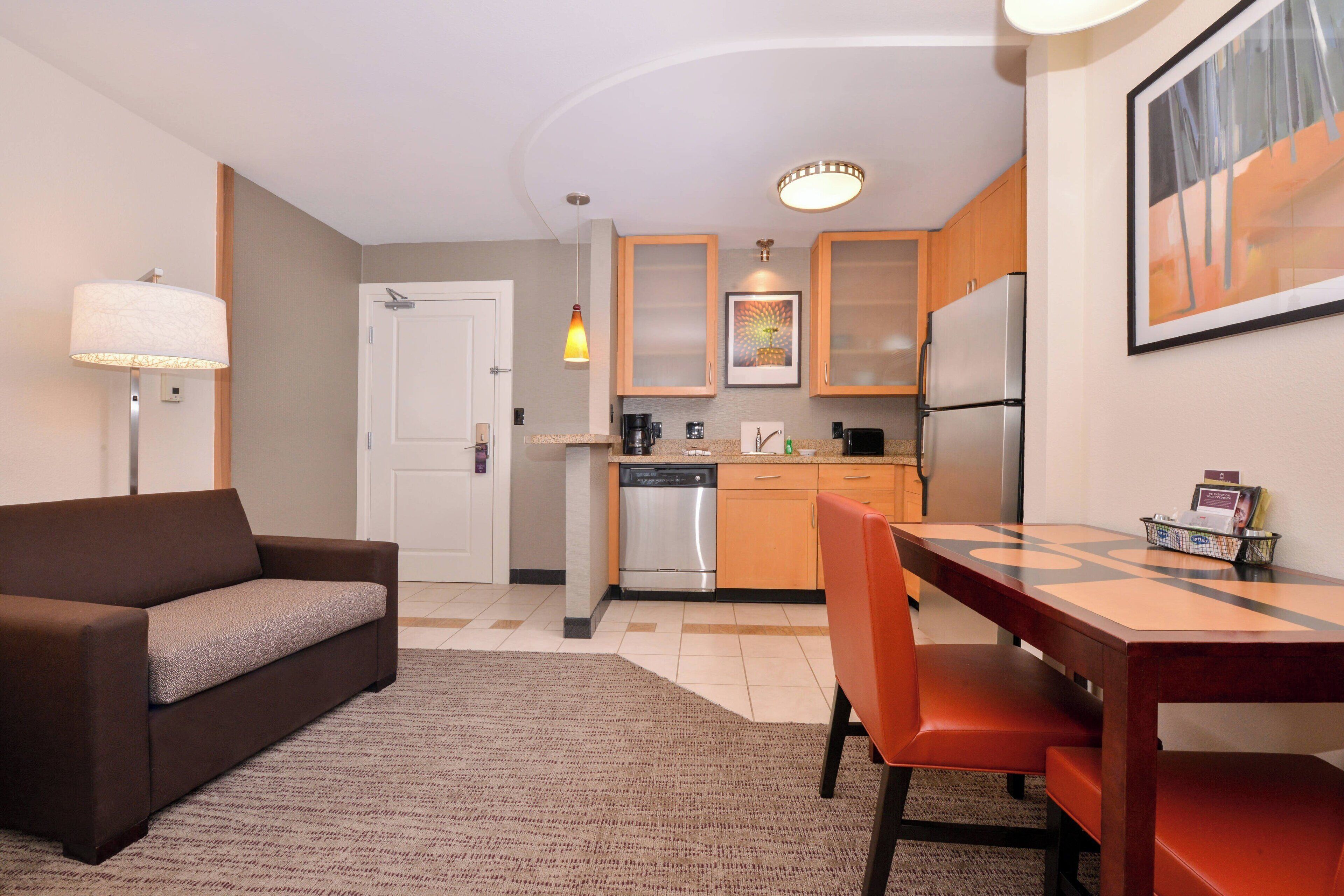 A compact living space with a sofa, dining table, chairs, kitchen area with appliances, and a door.