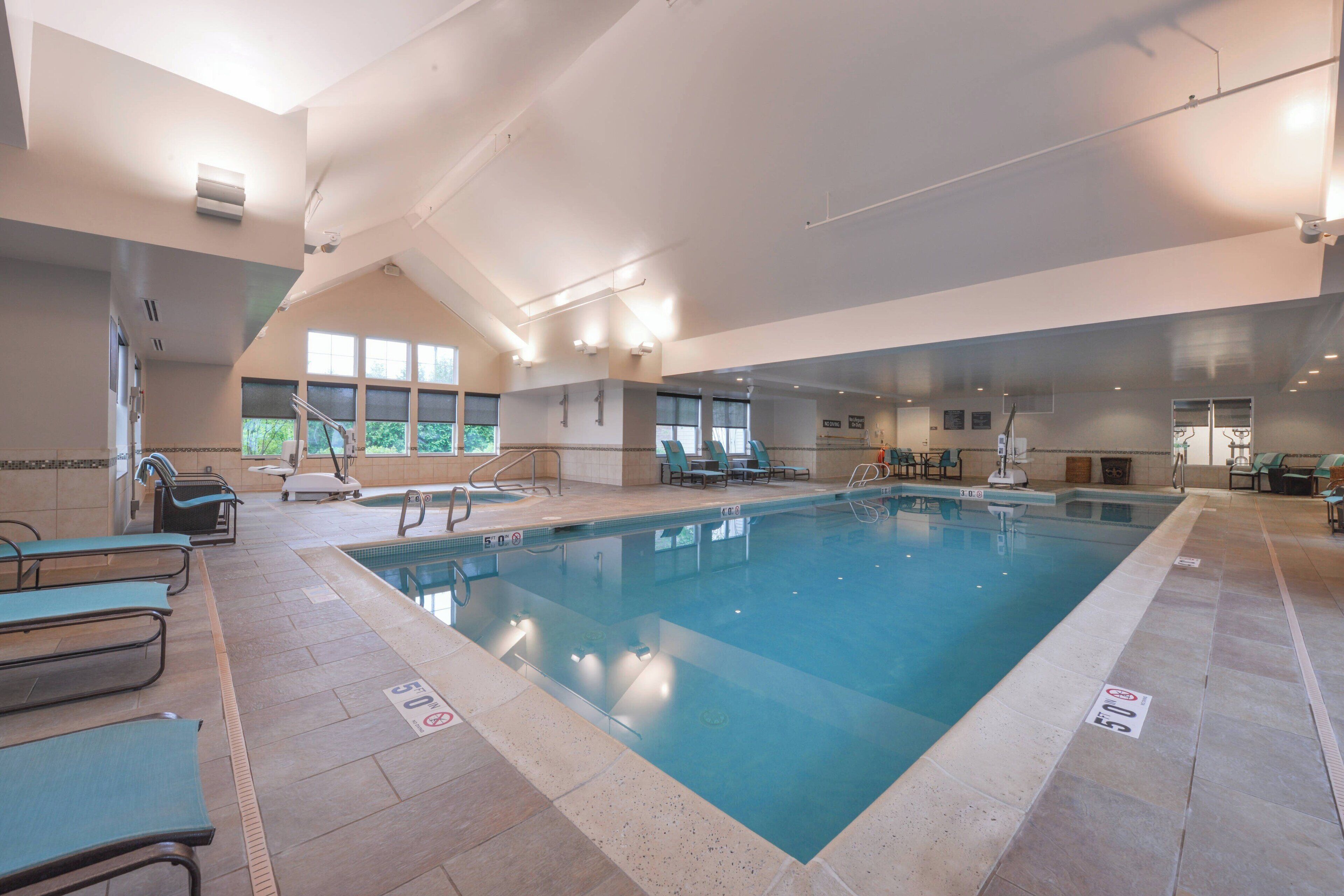 An indoor swimming pool with clear water, surrounded by lounge chairs and benches.