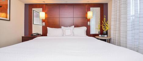 A large bed with a wooden headboard, two bedside lamps, and a nightstand with a phone.