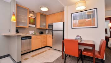 A compact kitchen with a refrigerator, microwave, and dishwasher. There is a dining area with a table and chairs.