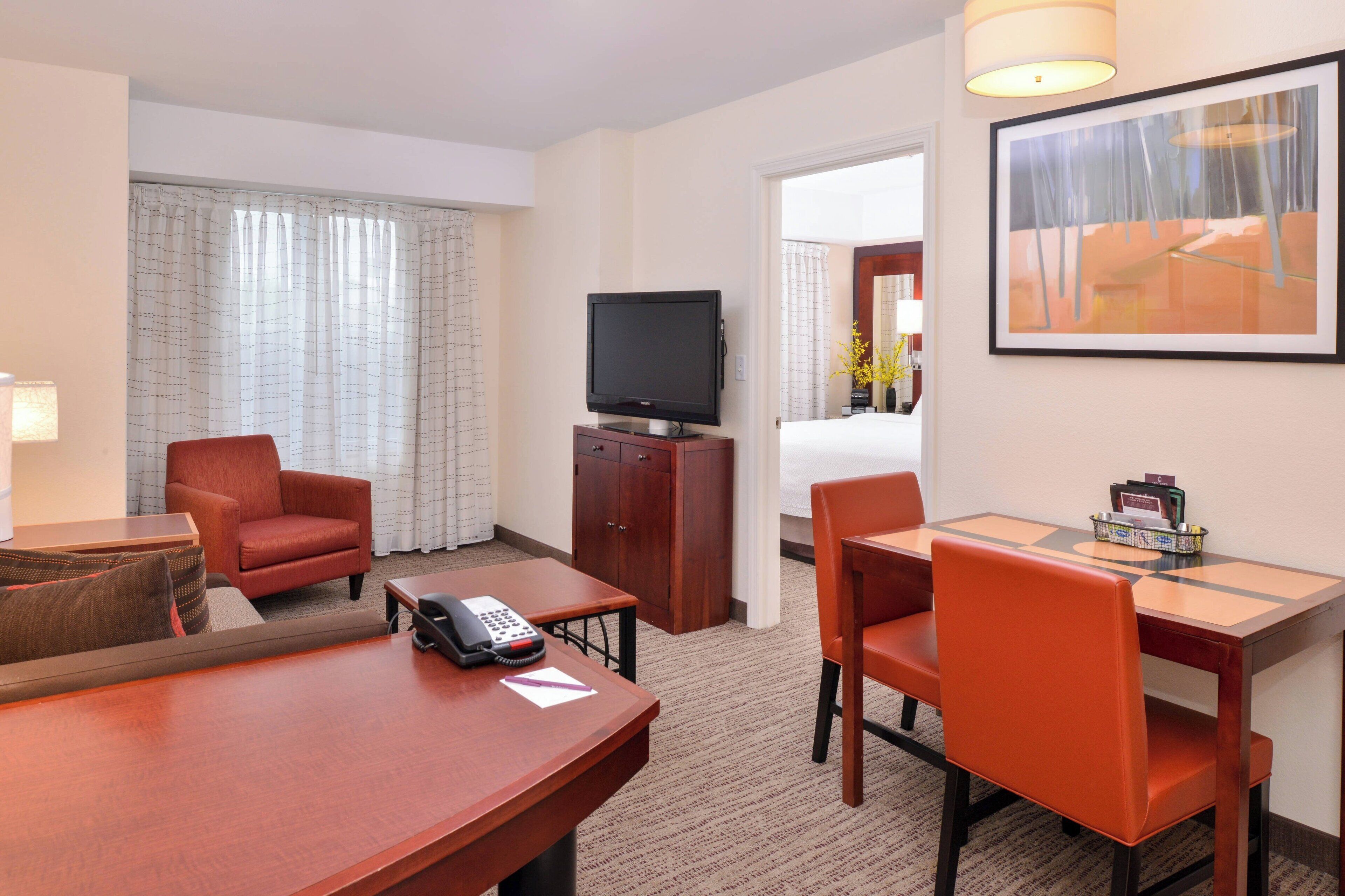 Ein Hotelzimmer mit Fernseher, Schreibtisch, zwei Stühlen, Telefon und Bett.