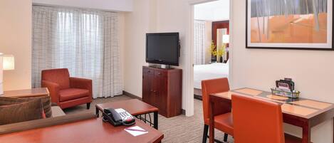 A hotel room with a TV, a desk, two chairs, a telephone, and a bed.