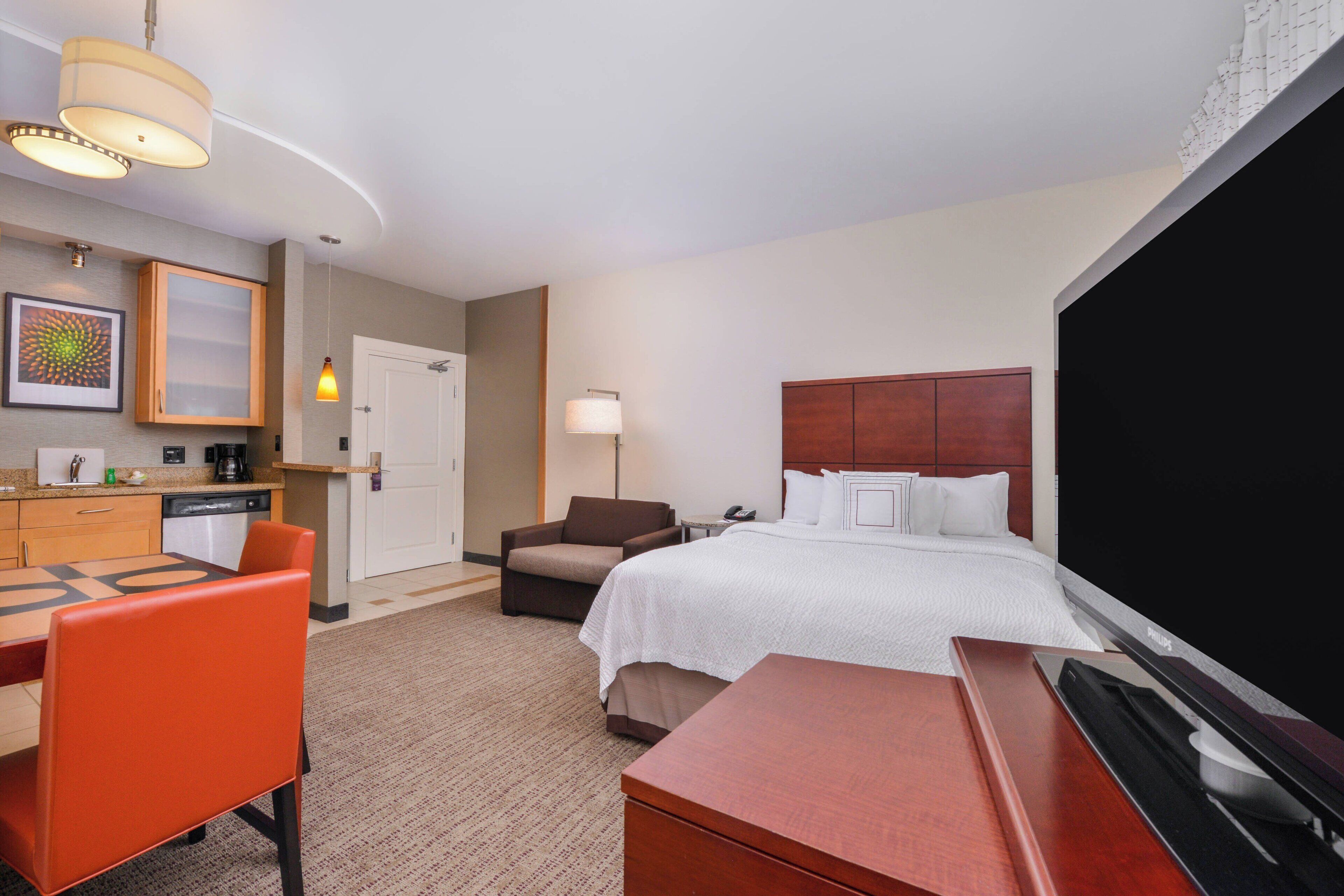 A hotel room with a bed, a desk, a chair, a television, and a kitchenette.