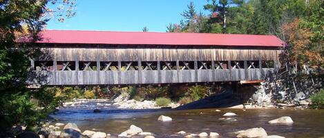 A wooden covered bridge over a river with rocks and trees.