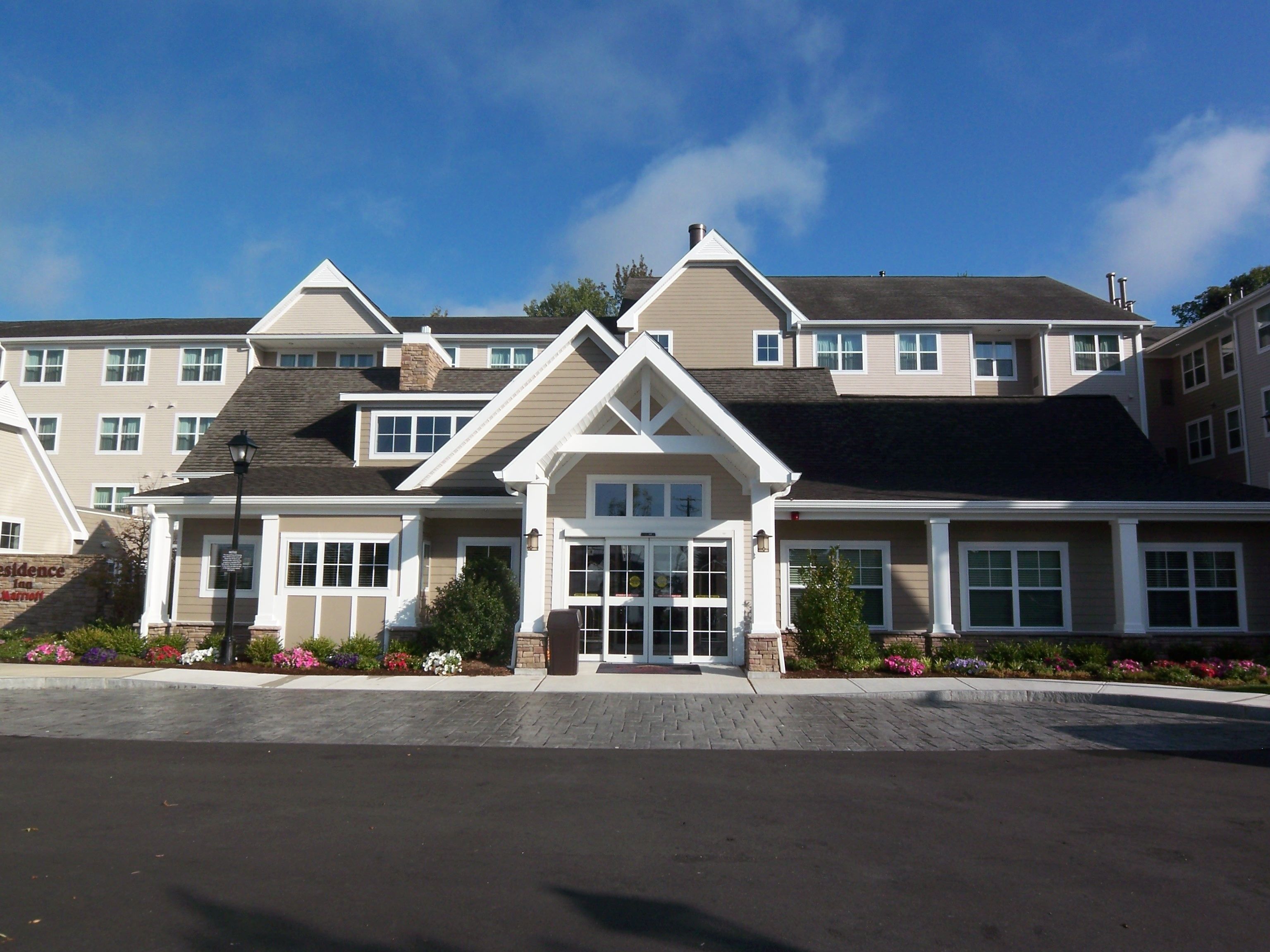 A multi-story hotel with a central entrance, large windows, and a brick pathway leading to the entrance.