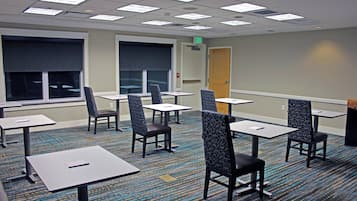 Una sala de conferencias con mesas y sillas, ventanas amplias y una puerta de salida.