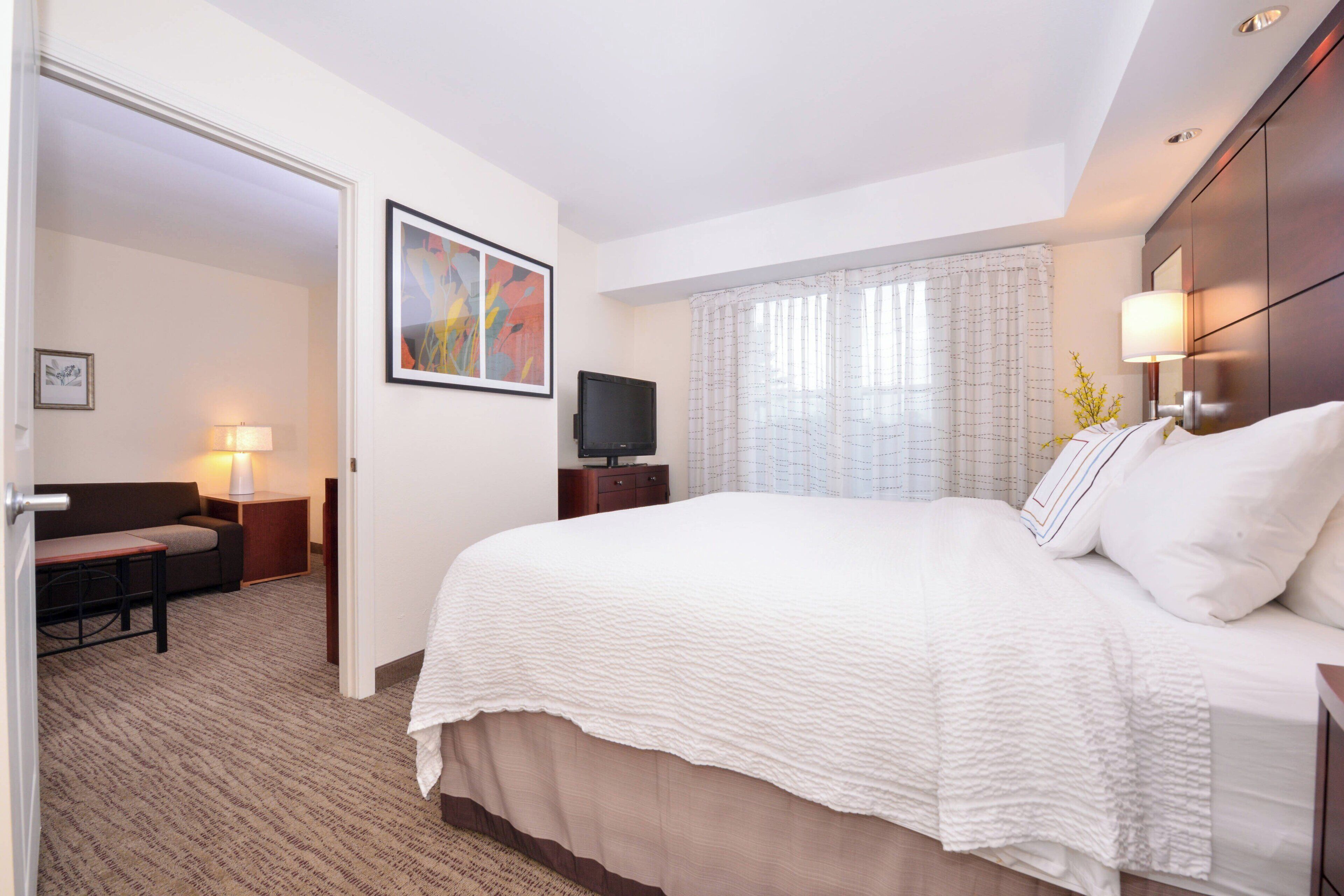 Una habitación de hotel con una cama grande, un escritorio, una silla, un televisor y una ventana con cortinas.