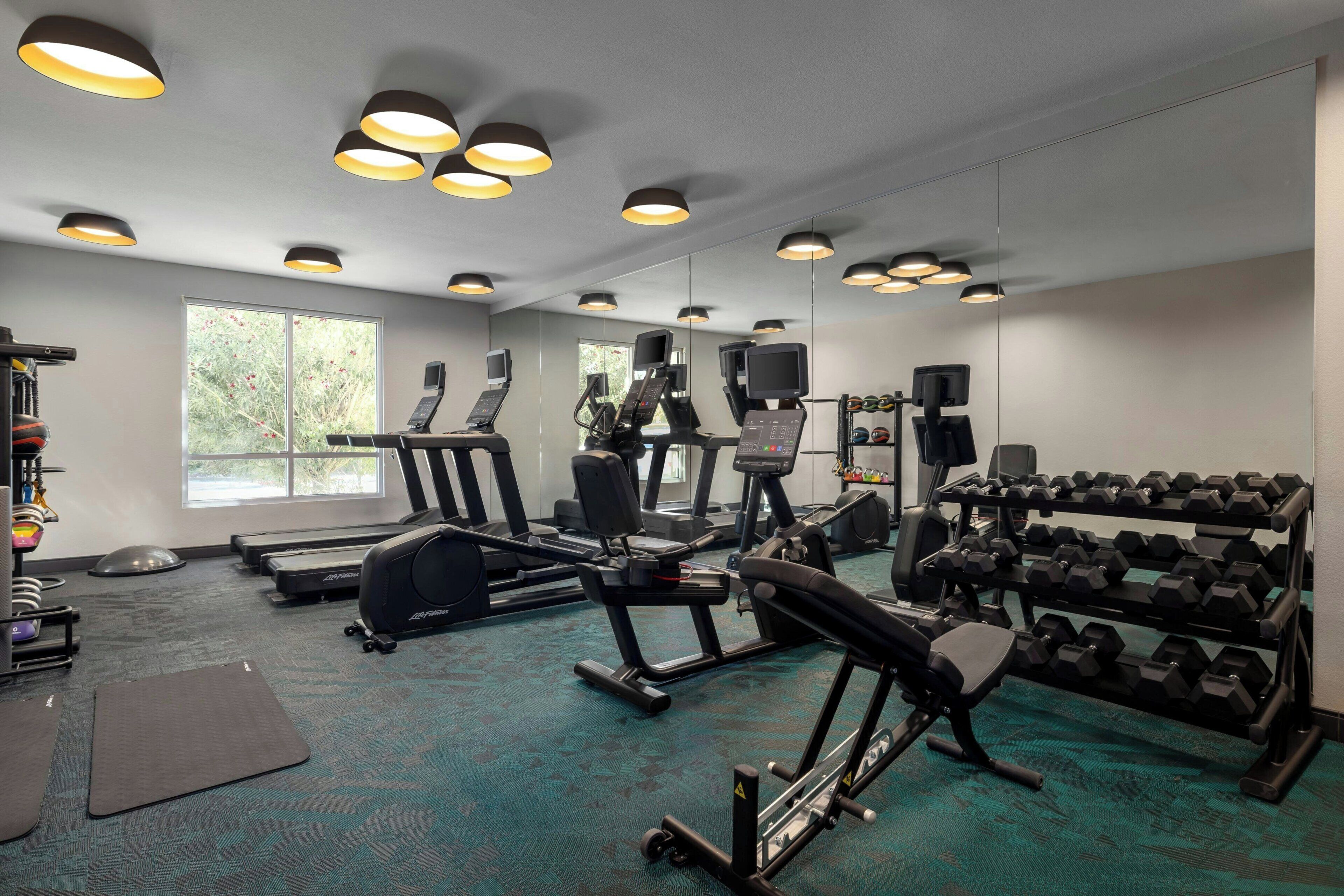 Une salle de sport équipée de tapis de course, d’appareils de musculation et d’haltères.