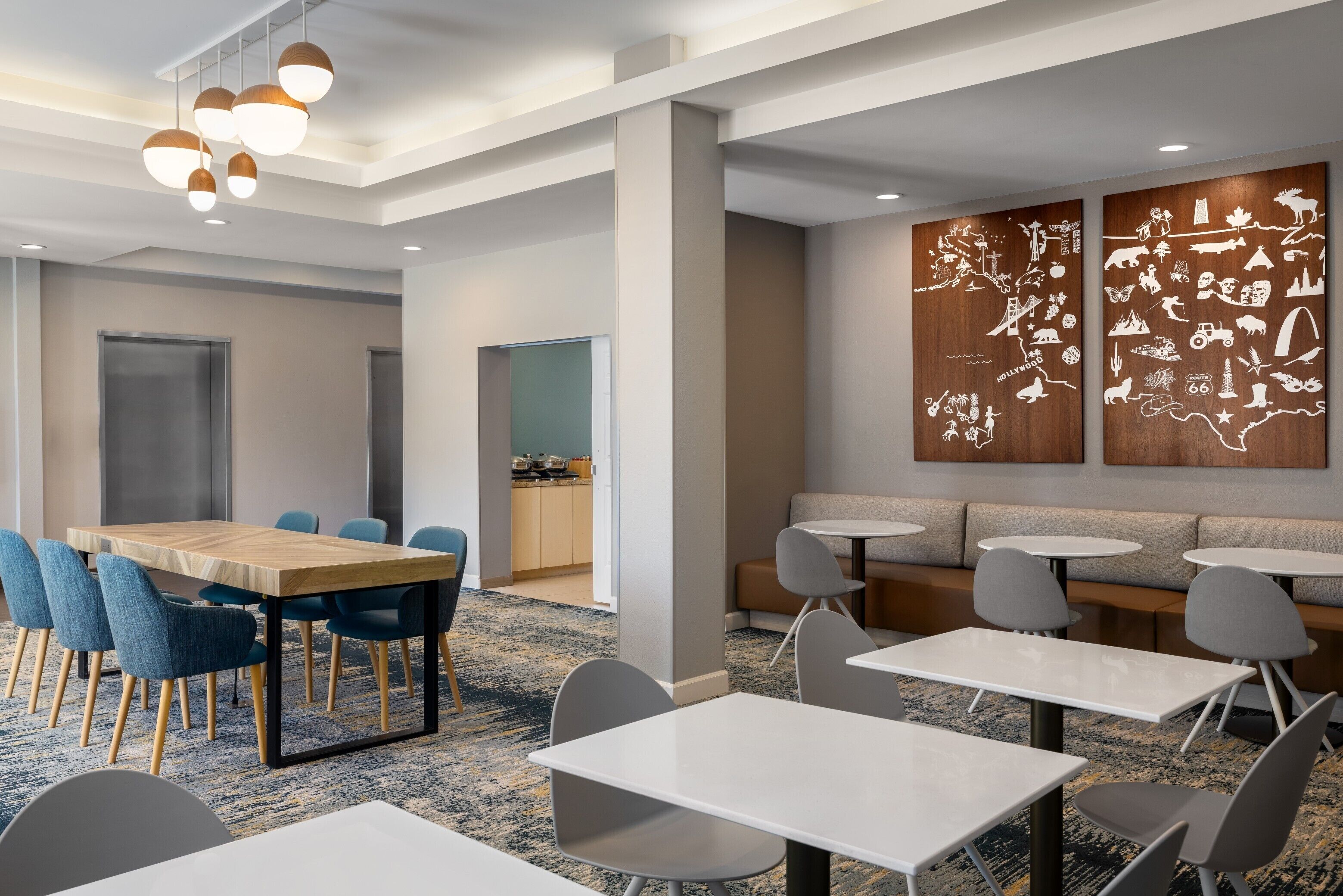 A modern conference room with a wooden table, blue chairs, and a seating area with gray sofas and round tables.
