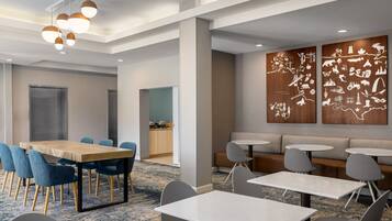A modern conference room with a wooden table, blue chairs, and a seating area with gray sofas and round tables.
