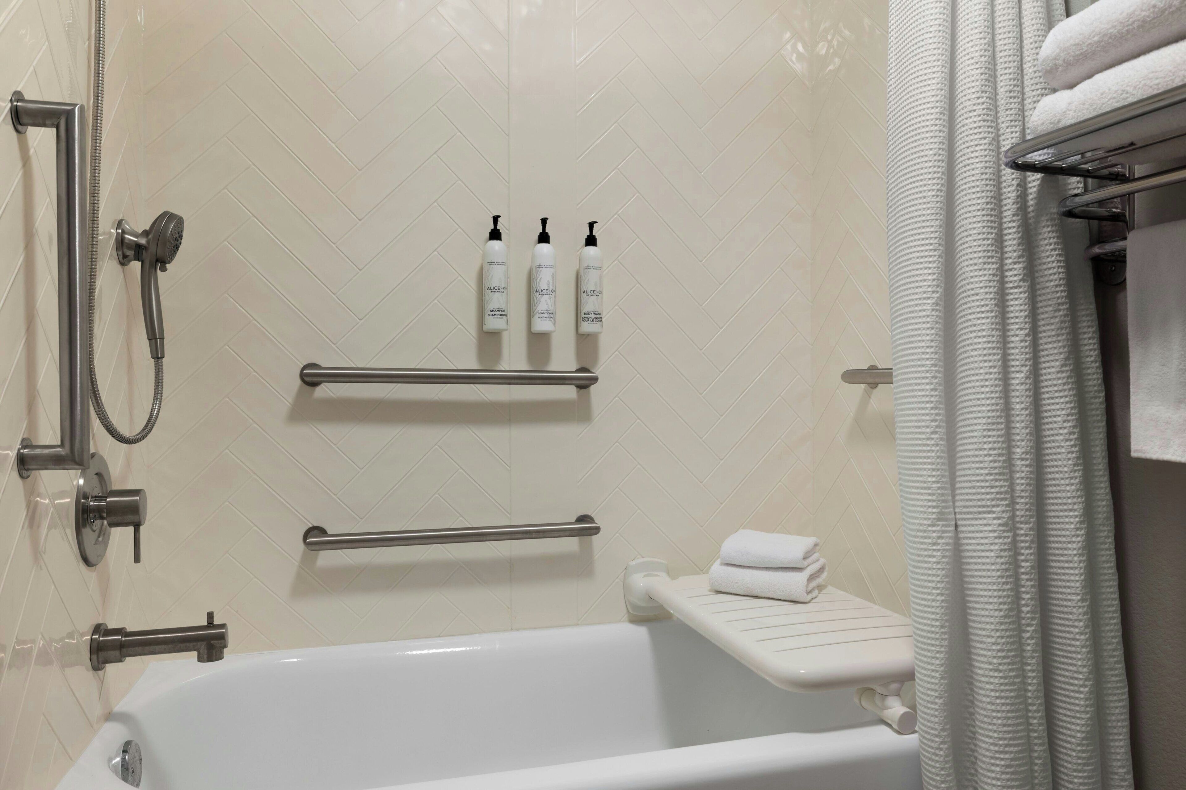 Ein Badezimmer mit Badewanne, Dusche und Toilette. Über der Toilette befindet sich ein Regal mit drei Flaschen.