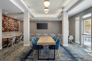 A conference room with a long table, blue chairs, a large screen, and a view of the outdoors. - TownePlace Suites by Marriott Goodyear (Goodyear)