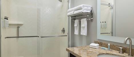 A modern bathroom with a glass-enclosed shower, a sink with a granite countertop, and a mirror above the sink.