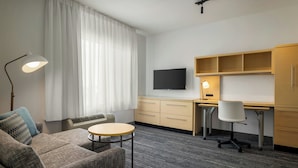 Ein Hotelzimmer mit einer Sitzecke, einem kleinen runden Tisch, einem Schreibtisch mit Stuhl, einem Fernseher und einer Lampe.