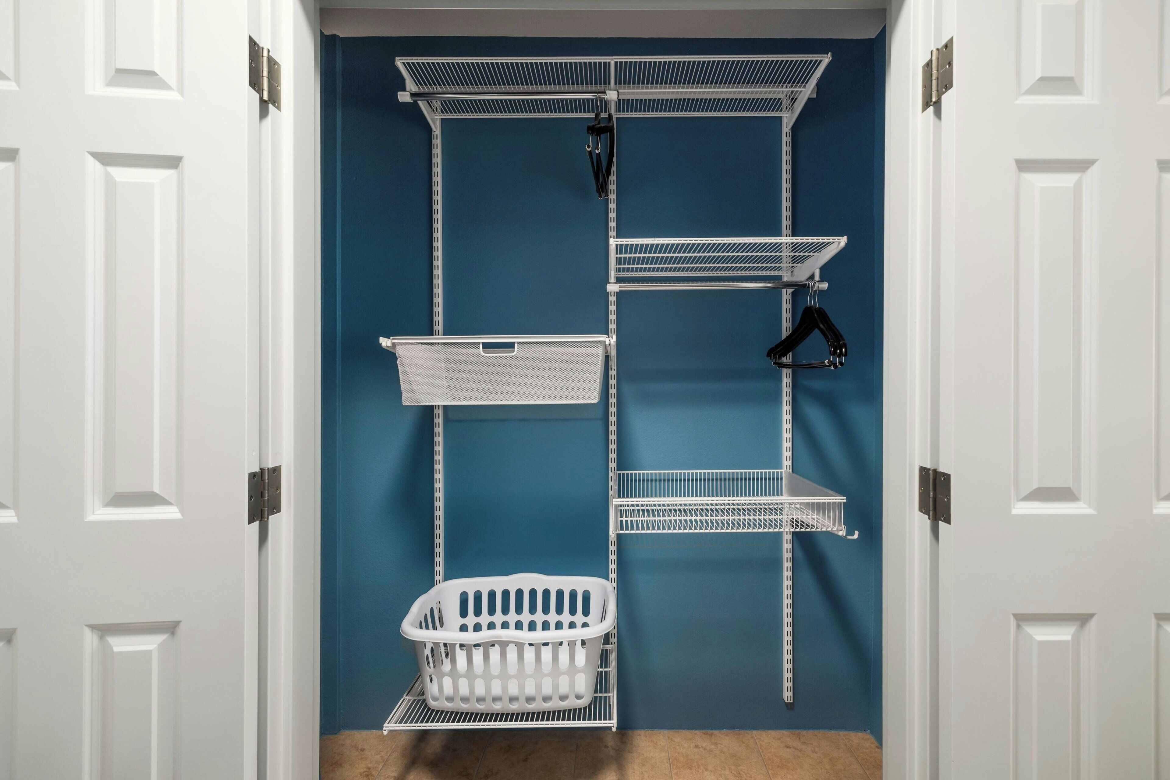 Un armario con puertas blancas, paredes azules y estanterías metálicas.