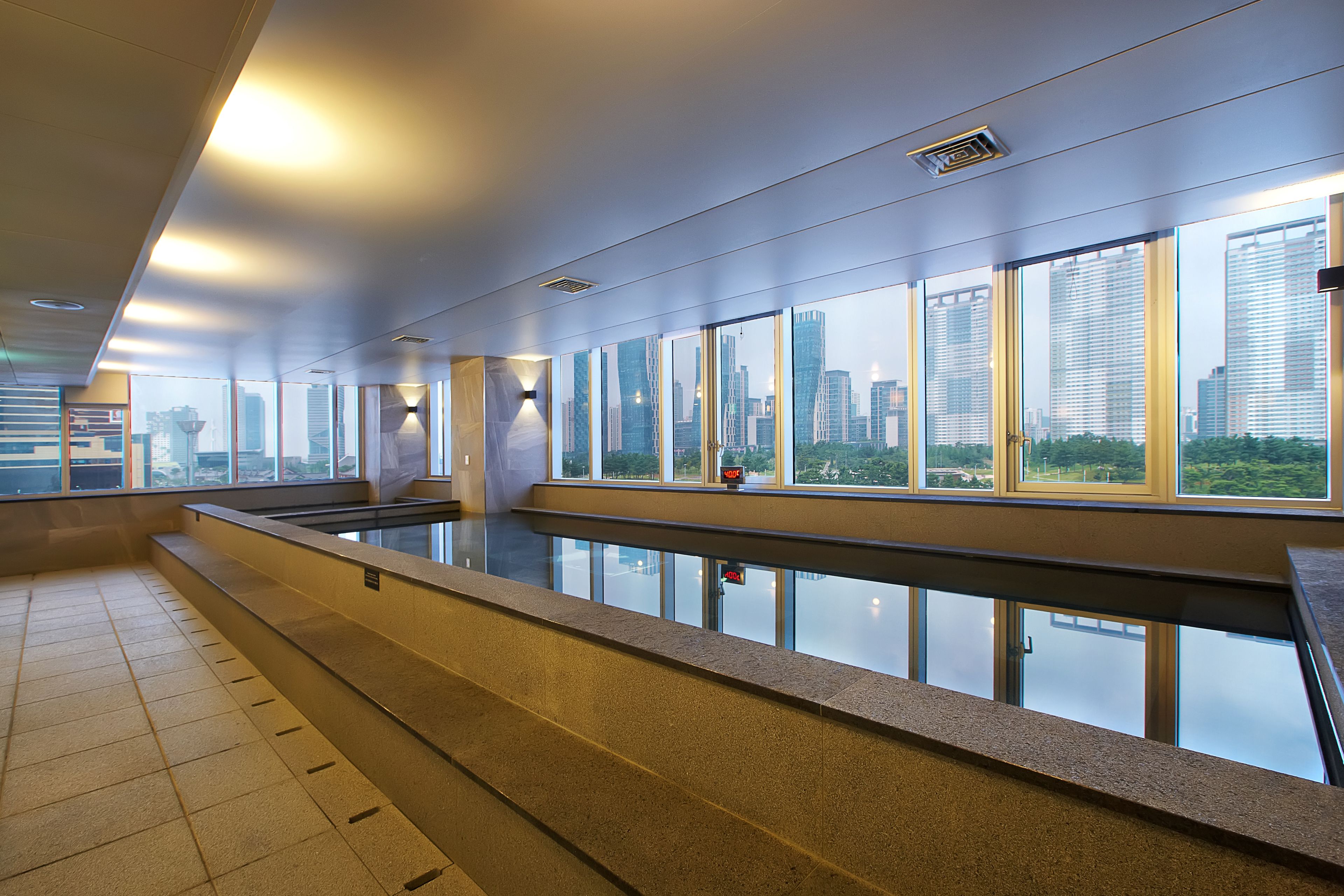 Une piscine intérieure moderne dotée de grandes baies vitrées offrant une vue sur la ville.