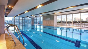 An indoor swimming pool with clear glass walls, a metal ladder, and a city view. - Orakai Songdo Park Hotel, BW Premier Collection (Incheon)
