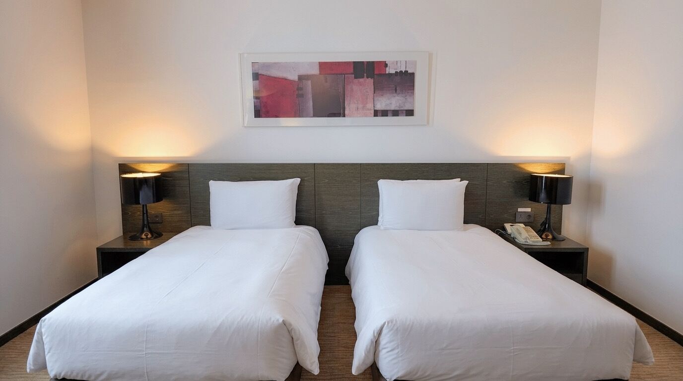 A hotel room with two single beds, a nightstand with a lamp, and a painting on the wall.