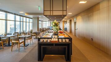 A modern hotel dining area with a buffet setup, large windows, and a clean, minimalist design.