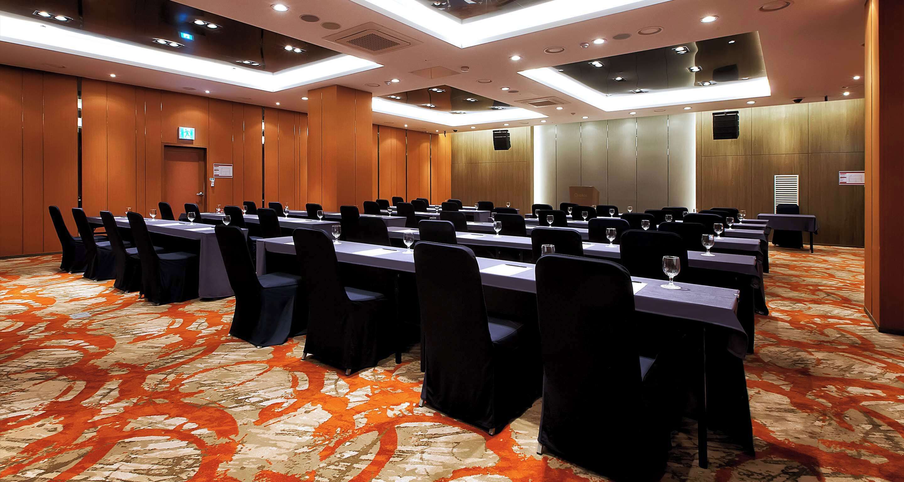 A conference room with multiple tables and chairs, equipped with glassware and documents, in a modern hotel setting.