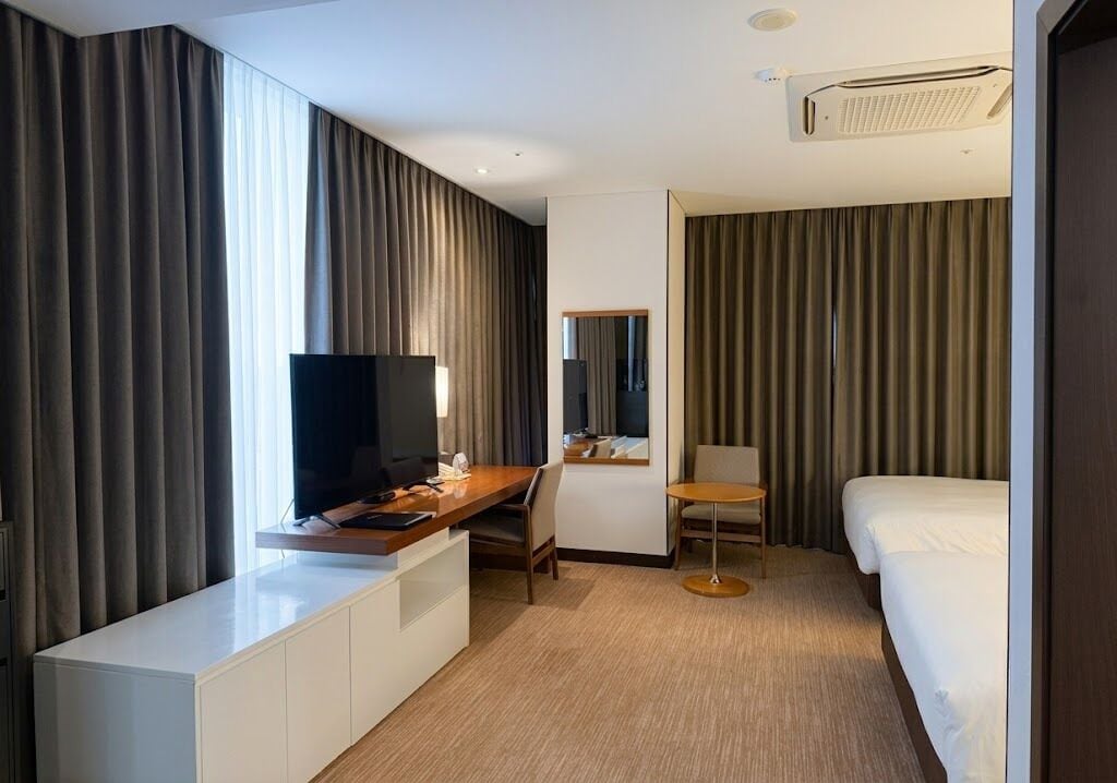 Een hotelkamer met een bed, een bureau met televisie, een stoel en een groot raam met gordijnen.