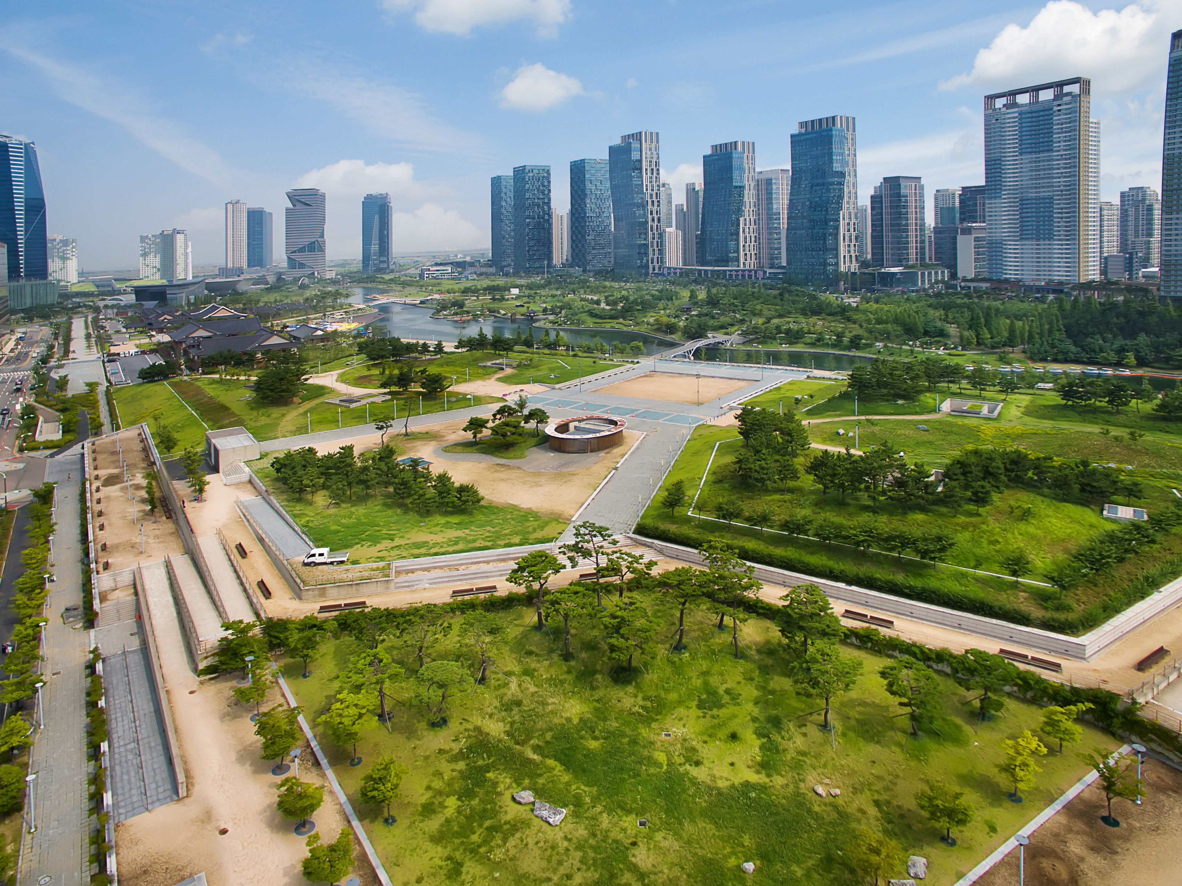 A modern urban park with green spaces, pathways, and a central circular plaza.