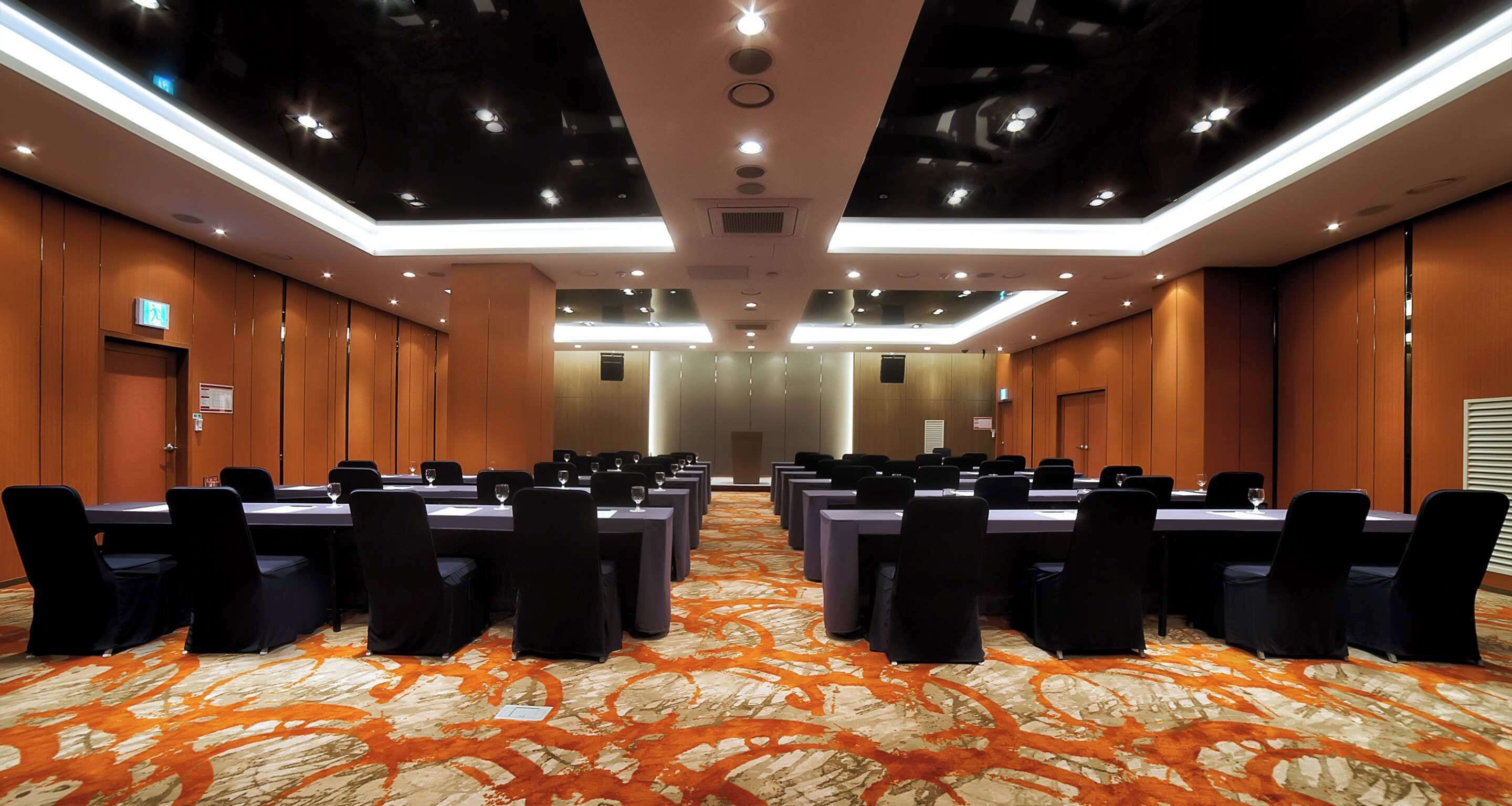 Un salón de conferencias con varias mesas y sillas, una alfombra estampada y un diseño de techo moderno.