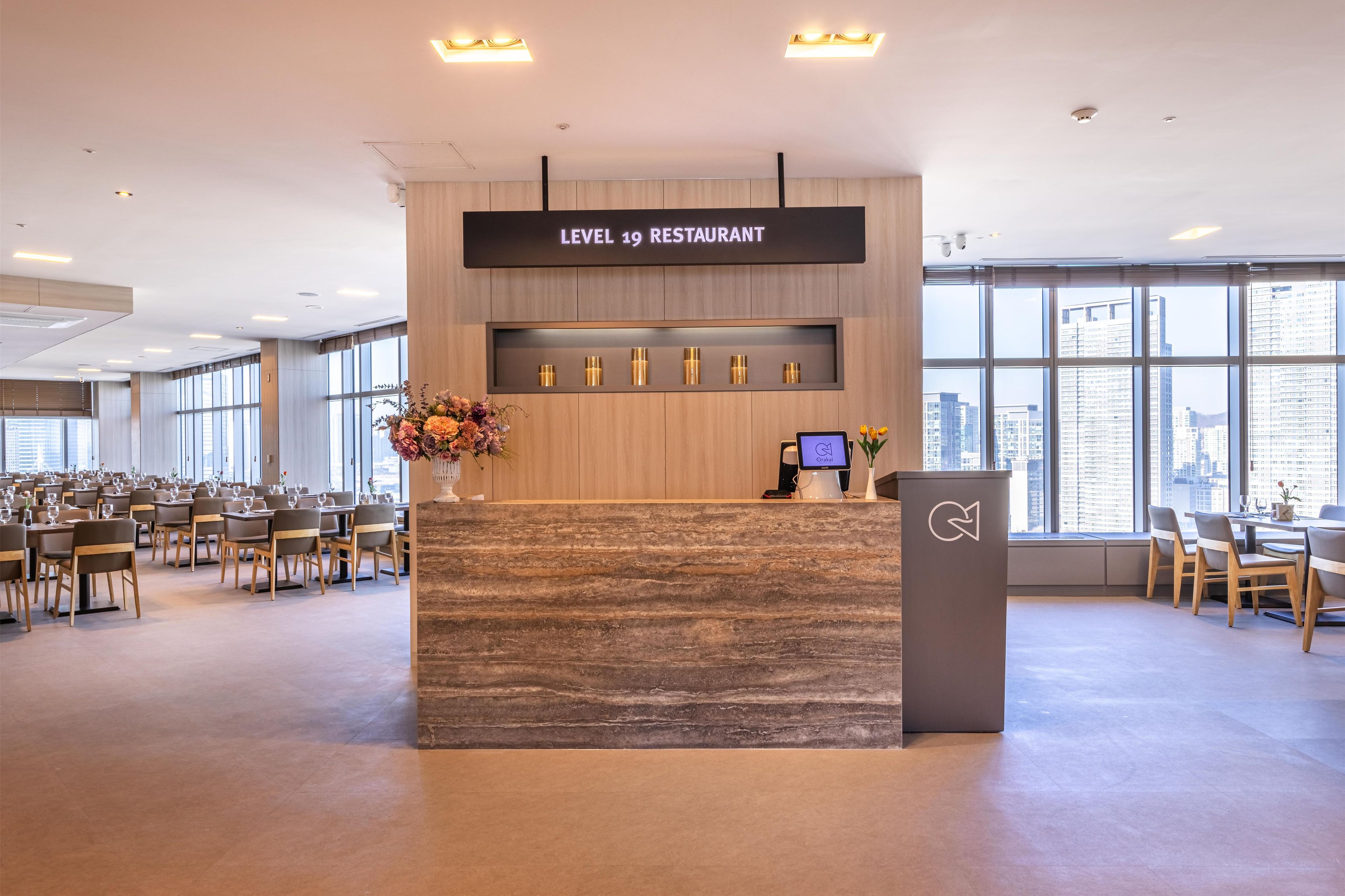 A reception area with a sign reading 'LEVEL 19 RESTAURANT' and a digital screen displaying 'Orakai'.