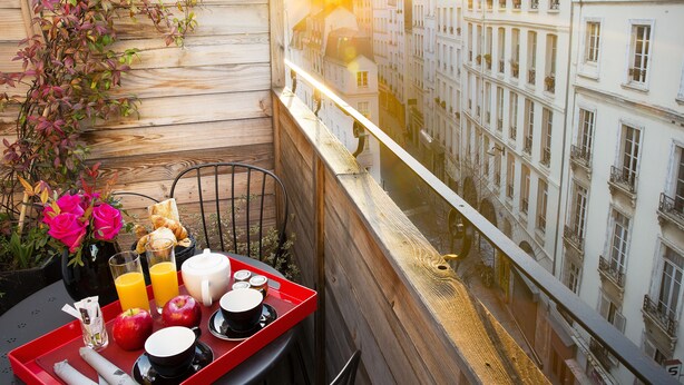 A balcony with a breakfast tray, flowers, and a view of a river and buildings. - Hotel Les Théâtres (Paris)