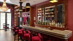 A bar area with red upholstered chairs, a long counter, and bookshelves filled with books. - Hotel Les Théâtres (Paris)