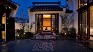 A traditional building with a tiled roof, a stone pathway leading to the entrance, and a small garden area with plants and a birdcage. - Banyan Tree Hangzhou (Hangzhou)