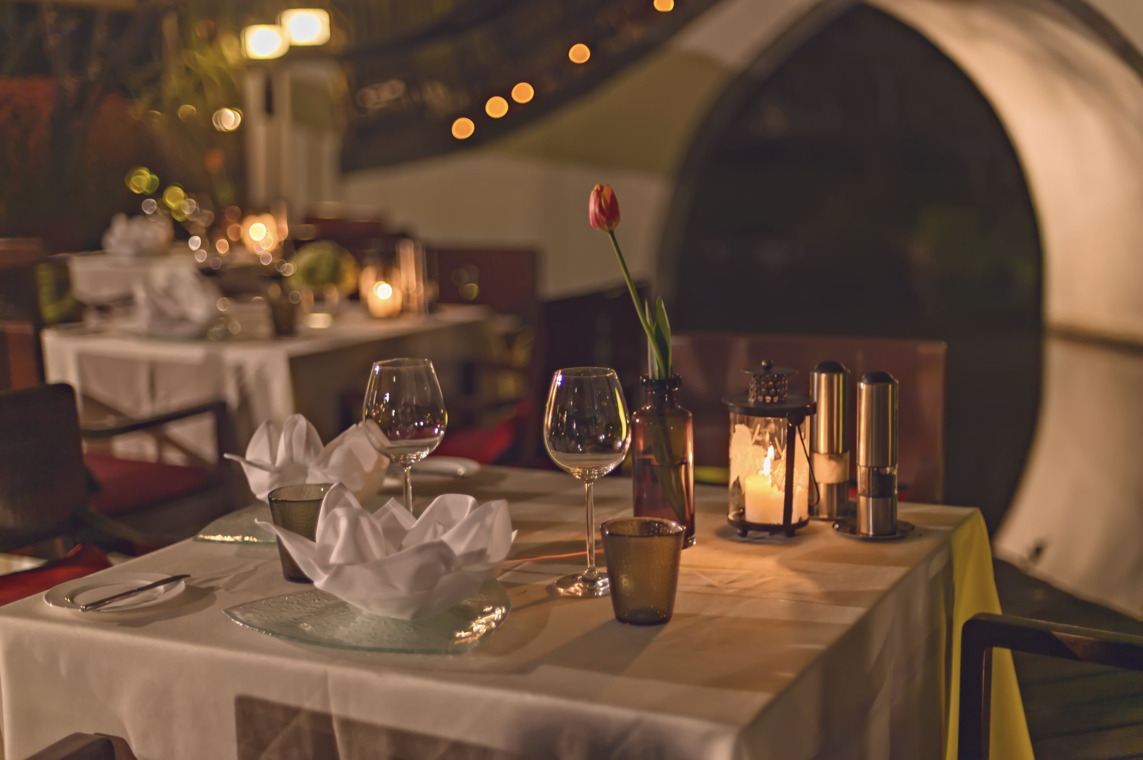Una mesa de comedor dispuesta con copas de vino, una vela y un florero con una sola tulipa.