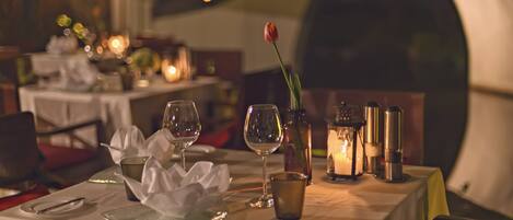 Una mesa de comedor dispuesta con copas de vino, una vela y un florero con una sola tulipa.