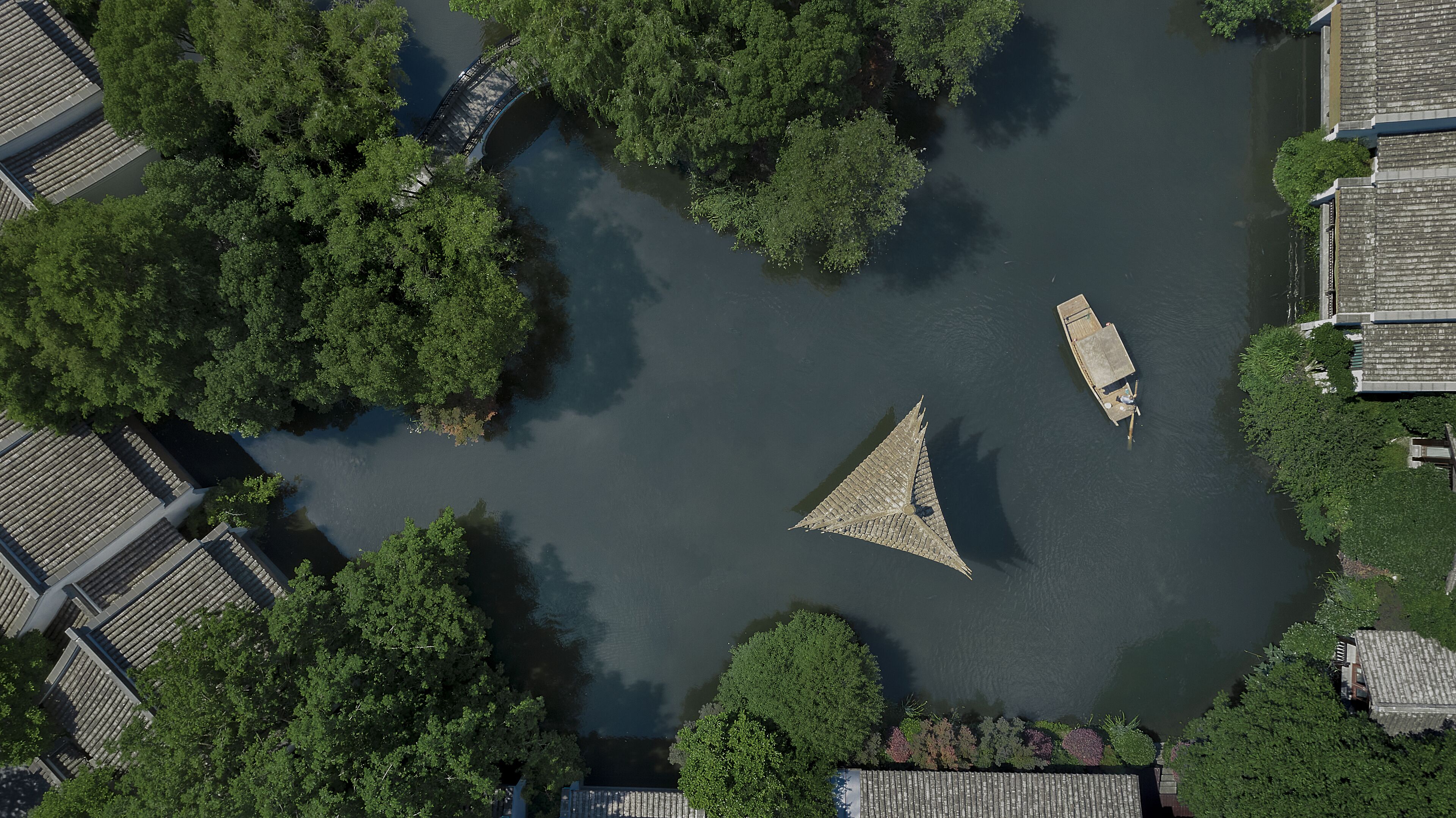 An aerial view of a river with boats, surrounded by dense greenery and traditional buildings.