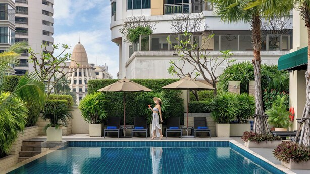 A swimming pool with clear blue water, surrounded by lounge chairs and umbrellas, with a cityscape in the background. - Marriott Executive Apartments Sukhumvit Park, Bangkok (Bangkok)