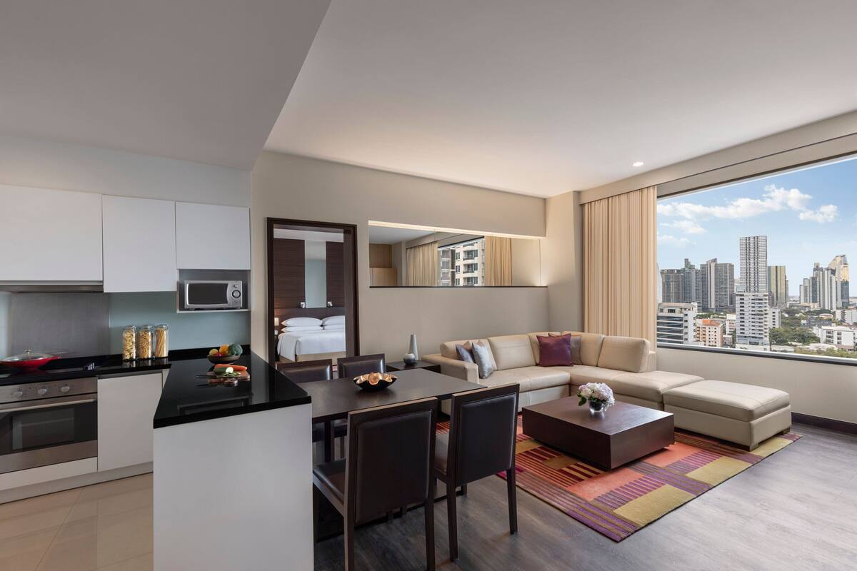 A modern apartment with a kitchen, dining area, and living room. It features a large window with a city view.
