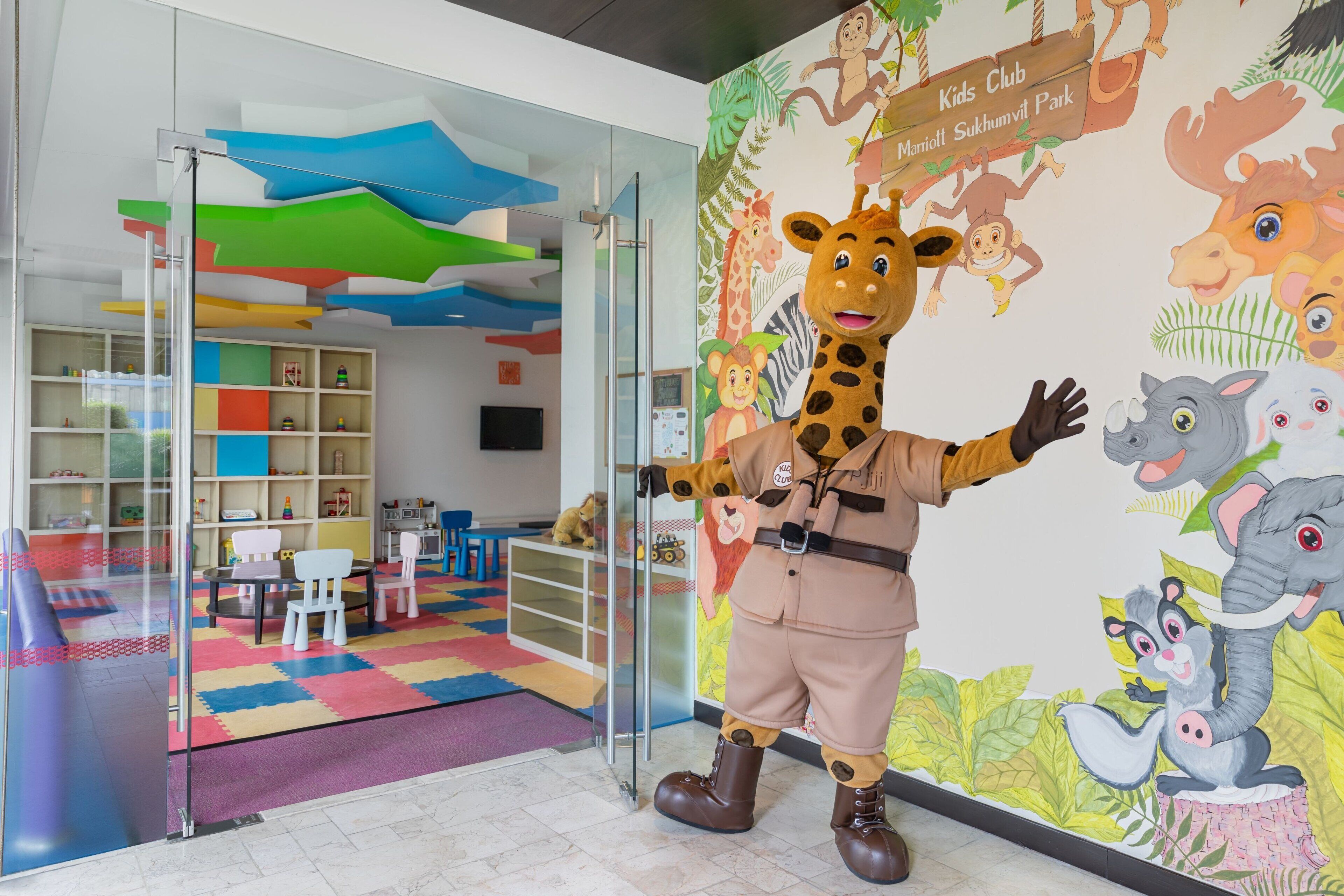 A children's play area with a mascot, colorful play mats, and a mural of jungle animals.